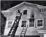 Firefighter at Top of Ladder Using Axe on House Window